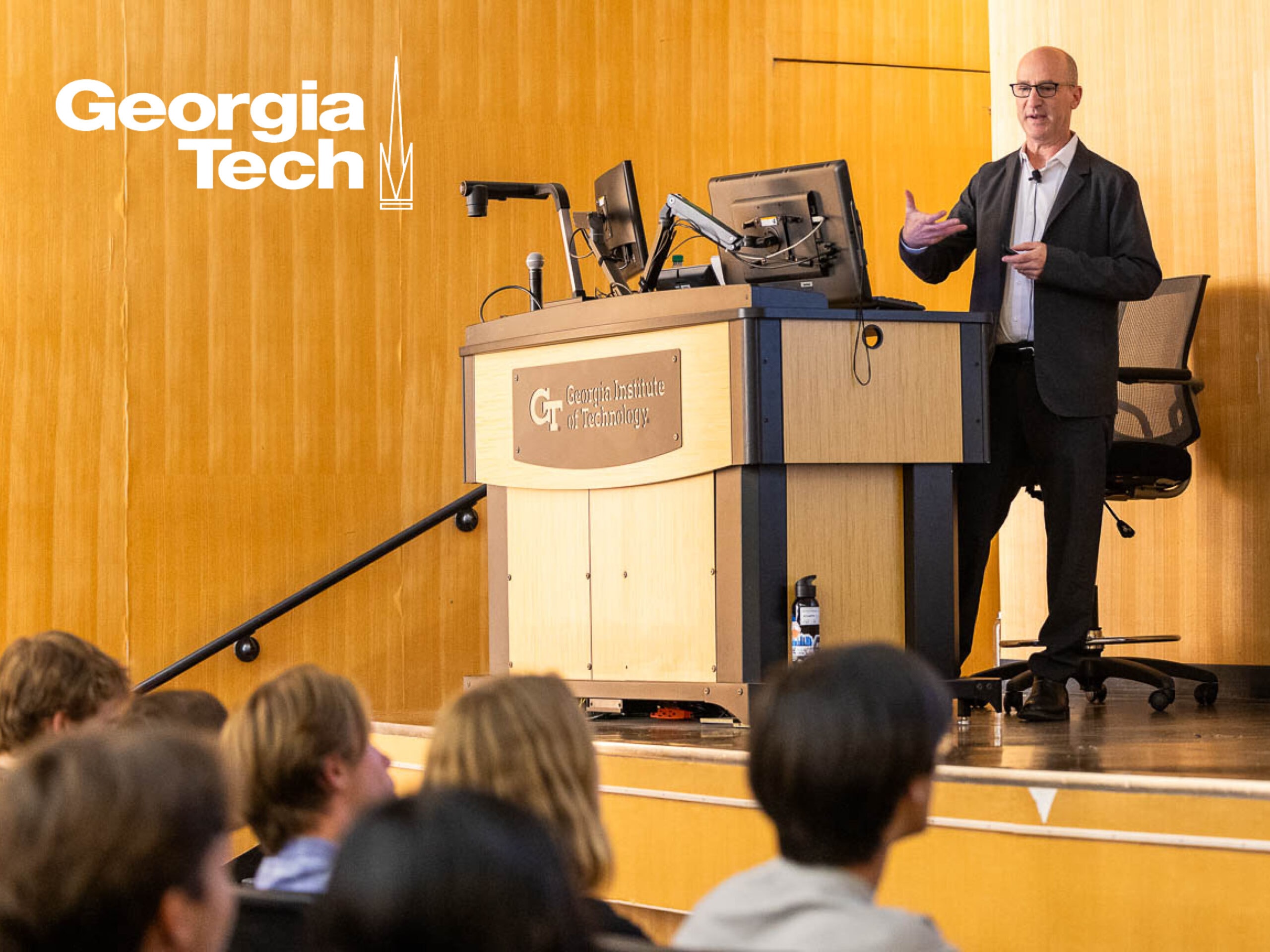 Photo of man lecturing on stage with podium, logo of Georgia Tech in the upper left corner