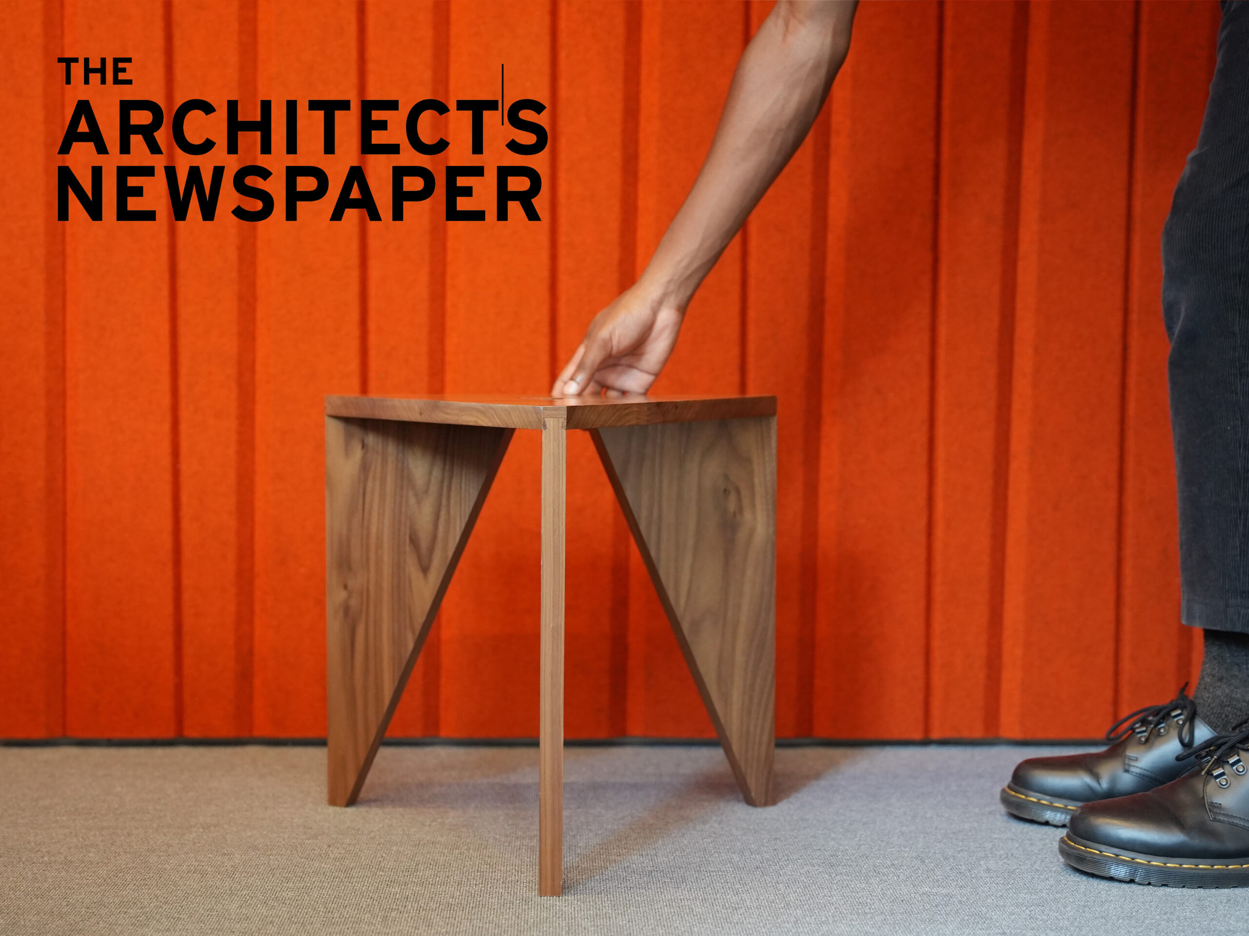 Triangular stool against orange felt background with the Architect's Newspaper logo in upper left corner